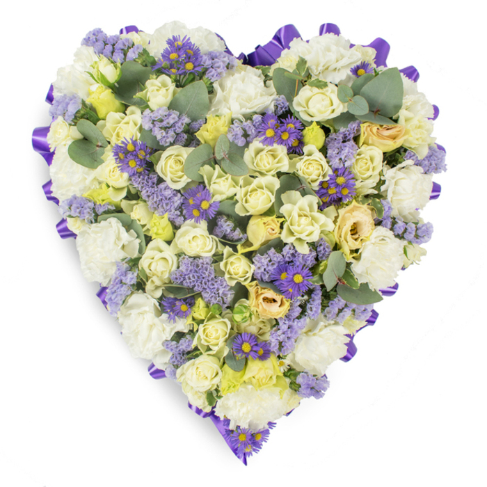 An exquisitely arranged heart of sympathy flowers set against a plain white backdrop, offering a study in soft pastels and refined texture. The outer edge is carefully finished with a continuous fold of deep purple satin ribbon, whose sheen frames the densely packed florals and gives the composition a formal, composed line. Filling the heart are clusters of cream and pale yellow roses, some held as compact buds and others opening to reveal layered petals with faint green undertones-these variations create a tactile landscape across the surface. Intermixed are voluminous, ruffled white carnations that lend the piece a traditional, comforting character, while the cooler tones are balanced by sprigs of lavender-hued statice whose fine, papery clusters bring air and delicacy to the design. Bright, small purple daisy-like flowers with clear yellow centers are scattered strategically to create visual rhythm and deeper color contrast. The rounded blue-green eucalyptus leaves are used sparingly but deliberately to break up density with their cool, silvery texture and to suggest a faint, refreshing scent. Bathed in soft, even light that highlights petal edges and ribbon folds, the tribute conveys a mood of serene remembrance, crafted for solemn occasions such as funerals or memorial services. Designed with the sensibilities of the local community in mind, this heart would sit gracefully at a service near Chingford Mount or be chosen for a thoughtful delivery to a family home in Walthamstow or Highams Park, communicating love, respect, and enduring memory through every carefully placed bloom.