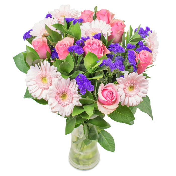 A carefully crafted arrangement from Chingford's talented florists, this bouquet in a clear glass vase captures the subtle luxury found in life's small celebrations. At the center, around seven to nine gently blushing pink roses unfurl with both youthful promise and classic beauty, their spiral petals ranging from tight buds to fuller blooms reminiscent of evening light falling on Chingford Mount. Nestled alongside, five to seven pale pink gerbera daisies display broad, layered petals with nearly white centers, creating a soft and welcoming harmony. Bright purple statice or limonium clusters are interspersed throughout, adding texture and a vivid splash of colour that brings contrast and depth, much like the vibrant blooms seen along local park edges. Lush, deep green foliage provides a verdant base, supporting the arrangement with a sense of abundance and freshness. The bouquet sits in a transparent vase, visible stems bathed in clear water, suggesting a freshly delivered gift for a loved one near Connaught Water or as a centrepiece for a family gathering. This elegant blend of roses, gerberas, and purple accents offers a timeless message-suited for occasions like birthdays, anniversaries, Mother's Day, or simply as a display of affection-conveying joy, gratitude, and heartfelt care, as only a true local Chingford bouquet can.
